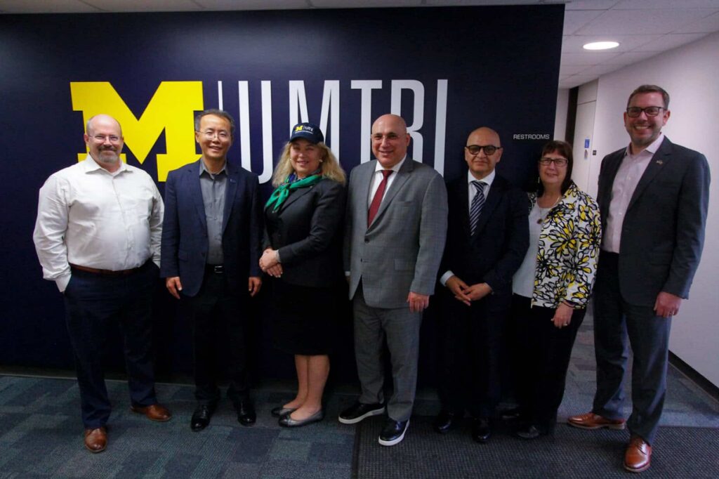Eric Wingfield, Henry Liu, Seval Oz, Firas Ibrahim, Hamid Ghasemi, Debby Bezzina, and Greg McGuire standing in front of the UMTRI sign